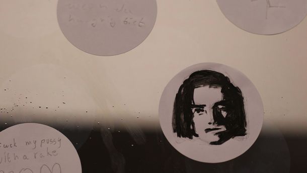 Foto: Runde Sticker auf einer Glasplatte. Auf einen Sticker ist ein Portrait gezeichnet.