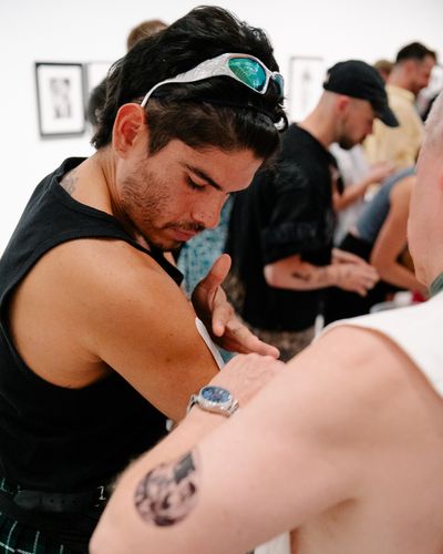 Photo: Scenes from the event, showing people either gathered around a long table with stick-on tattoos, in the foyer or in the outdoor area of the Berlinische Galerie.