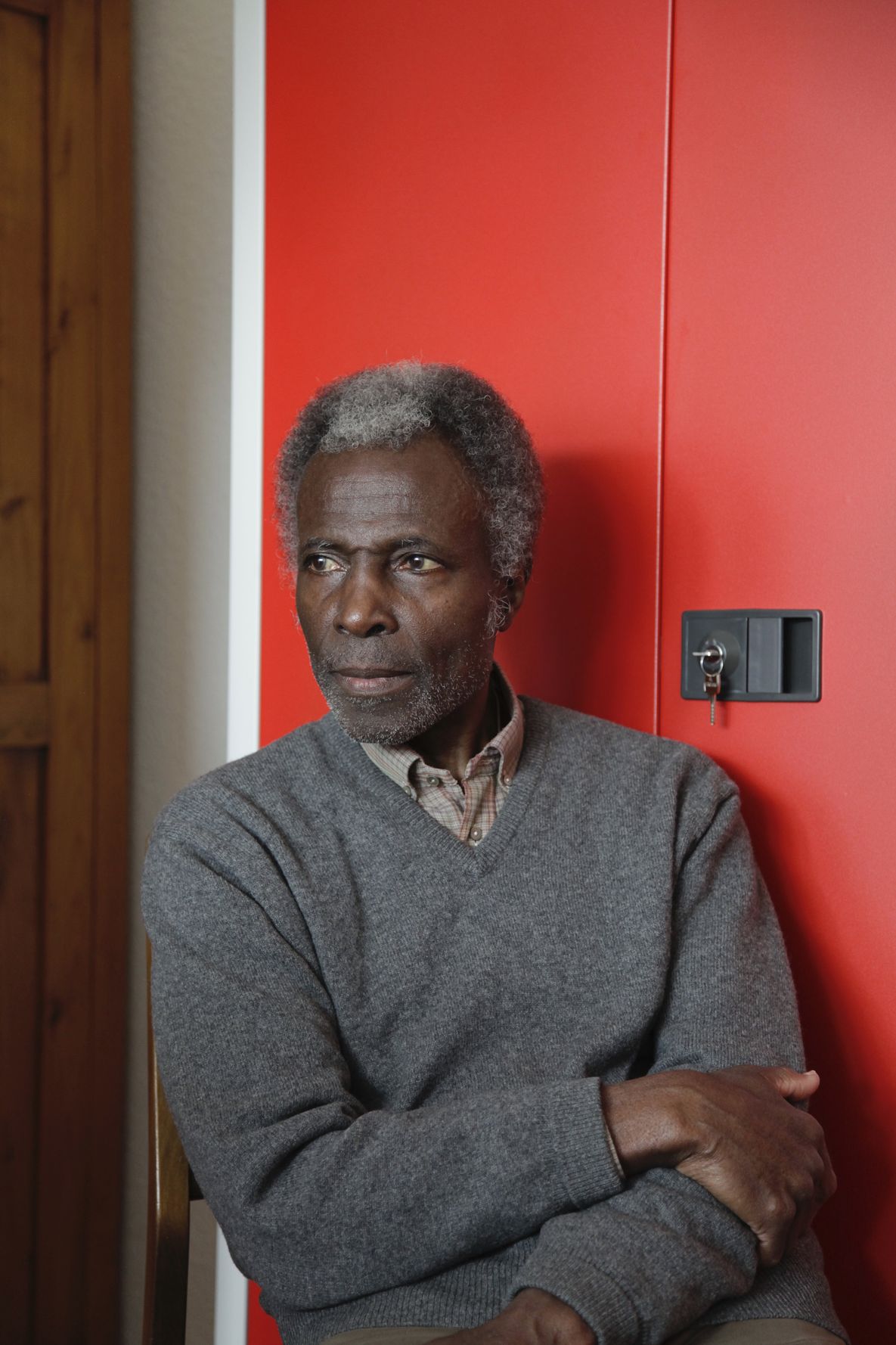 A person is leaning against a red and white metal cupboard. The person is wearing a grey jumper, has one arm draped over the other and is looking to the side.