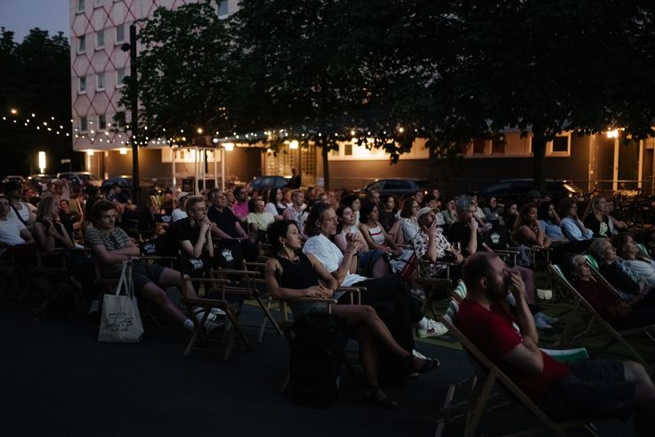 Open Air Video Art vor der Berlinischen Galerie Foto: Viele Menschen sitzen in Stuhlreihen auf dem Vorplatz der Berlinischen Galerie und blicken nach vorne auf eine Leinwand, die nicht auf dem Bild zu sehen ist. Es dämmert langsam.