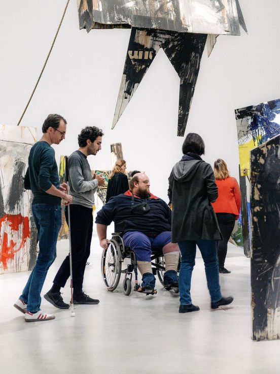 Photo: People move around in a room filling installation. One person with a wheelchair, one person with a white cane.