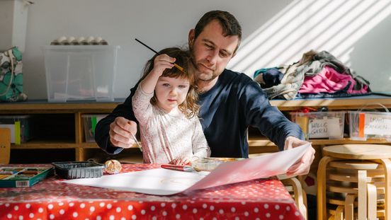 Foto: Erwachsene Person und Kind sitzen an einem Tisch. Sie malen gemeinsam ein Bild.