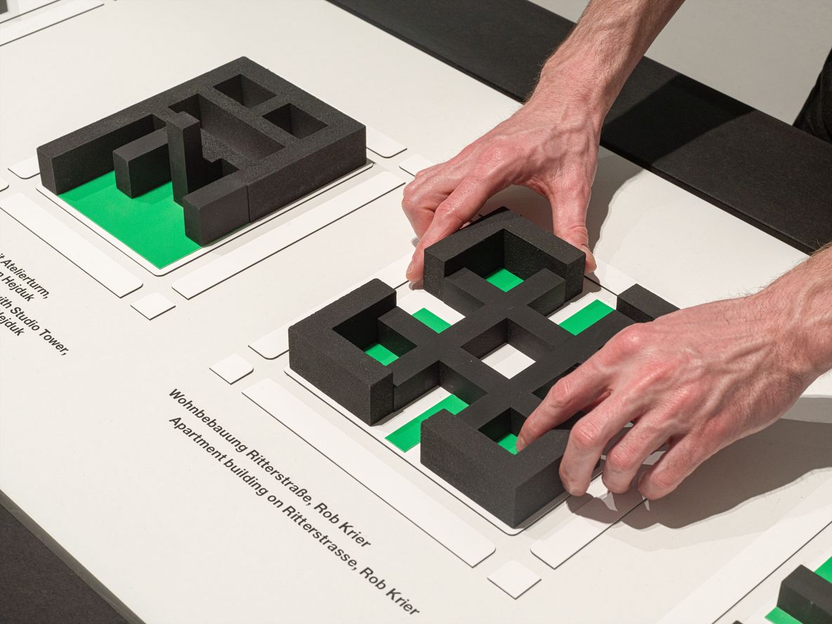 Museum-Berlin_Barrierefreiheit_Tastmodell_Anything-Goes Zwei Hände bestasten Tastmodell aus schwarzen Blöcken auf weißem Grund mit grünen Flächen.