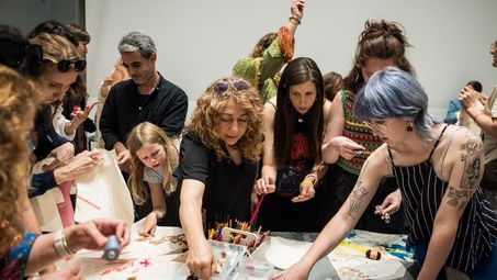Foto: Einige Personen stehen um einem Basteltisch, auf dem viele Materialien liegen.