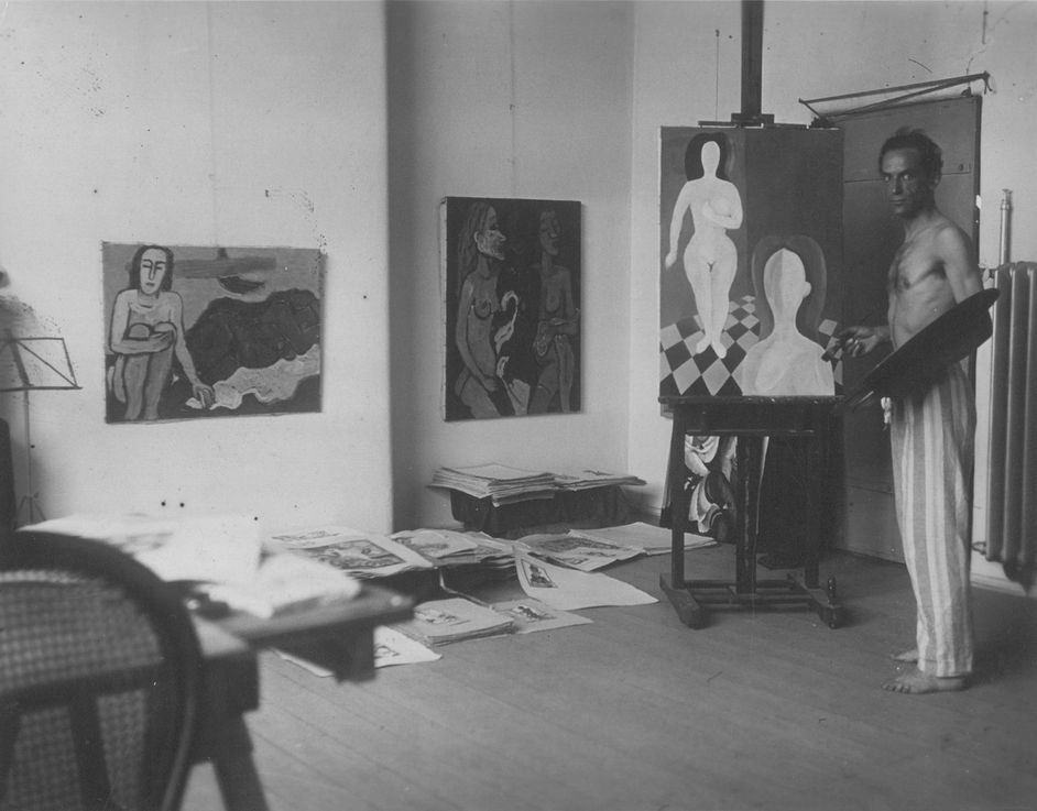 Schwarz-Weiß-Fotografie: Mann steht vor Gemälde auf Staffelei, an der Wand hinter ihm weitere Gemälde