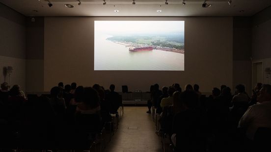 Foto: Blick auf eine Leinwand, auf der gerade ein Film gezeigt wird. Davor sitzen viele Menschen in Stuhlreihen.