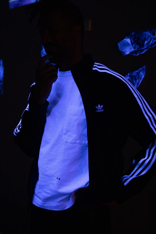 Foto: Close-Up einer Person mit Trainingsjacke und weißem Tshirt unter Schwarzlicht.