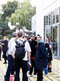 Foto: Auf dem Vorplatz der Berlinischen Galerie stehen einige Menschen in kleineren Gruppen zusammen und unterhalten sich miteinander. Eine Person blickt direkt in die Kamera.