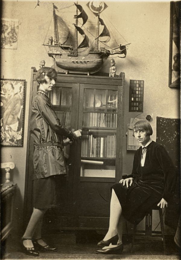 Unbekannte*r Fotograf*in, Mimi (links) stehend und Jeanne (rechts) sitzend vor dem Bücherschrank in ihrem Berliner Atelier Kudamm 29, Berlin, um 1920