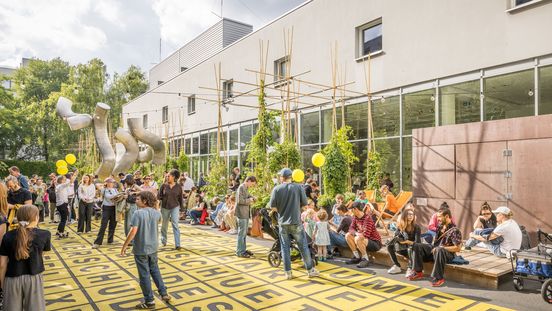 Foto: Seitenansicht der Berlinischen Galerie. Daneben sitzen, stehen oder laufen viele Menschen über den Vorplatz des Museums oder zwischen Pflanzenkübeln, die auf einer Holzplattform neben dem Gebäude platziert sind.