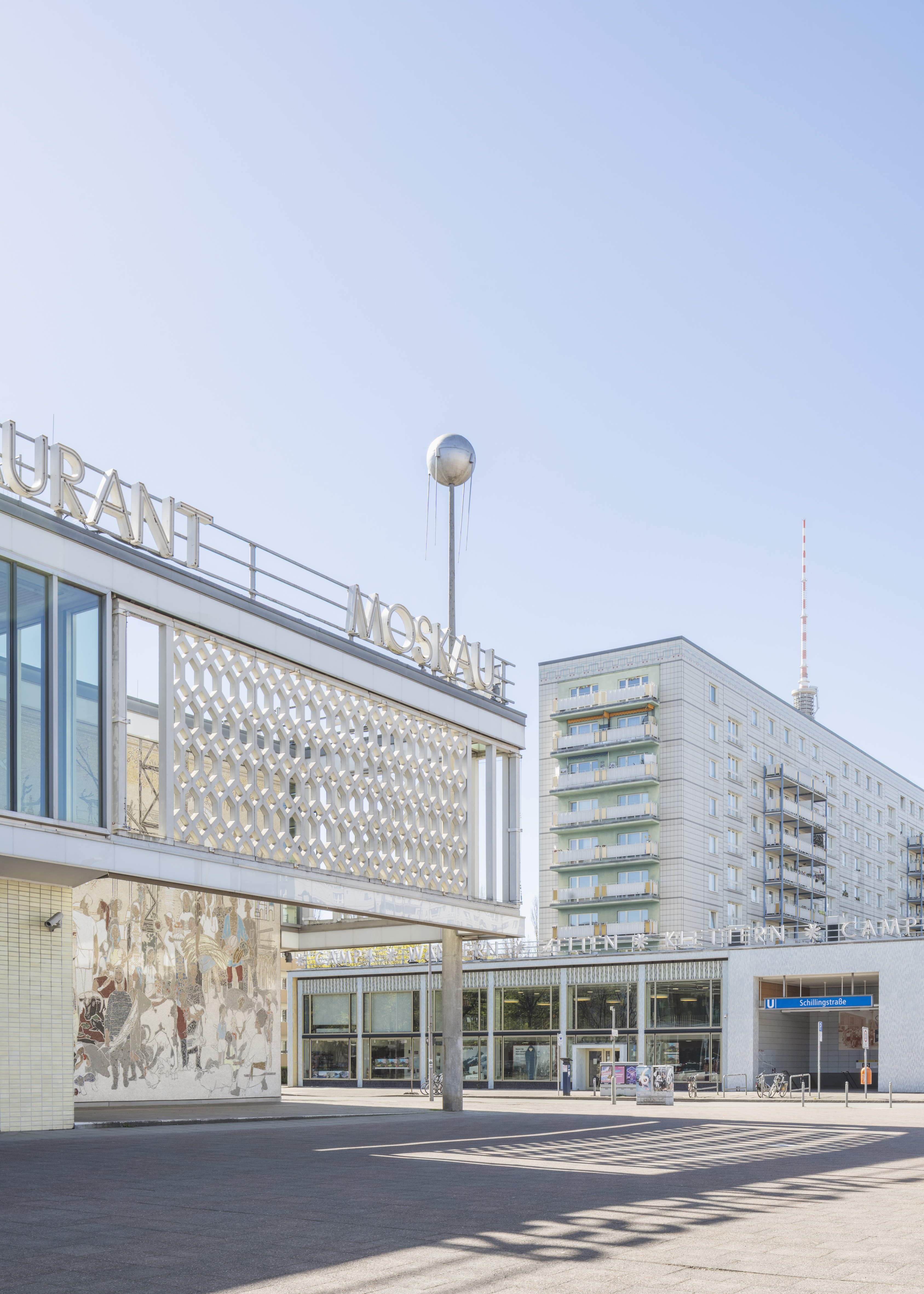Ansicht des Café Moskau in Berlin mit dem Schriftzug „MOSKAU“, ornamentaler Fassade und umliegender DDR-Architektur unter blauem Himmel