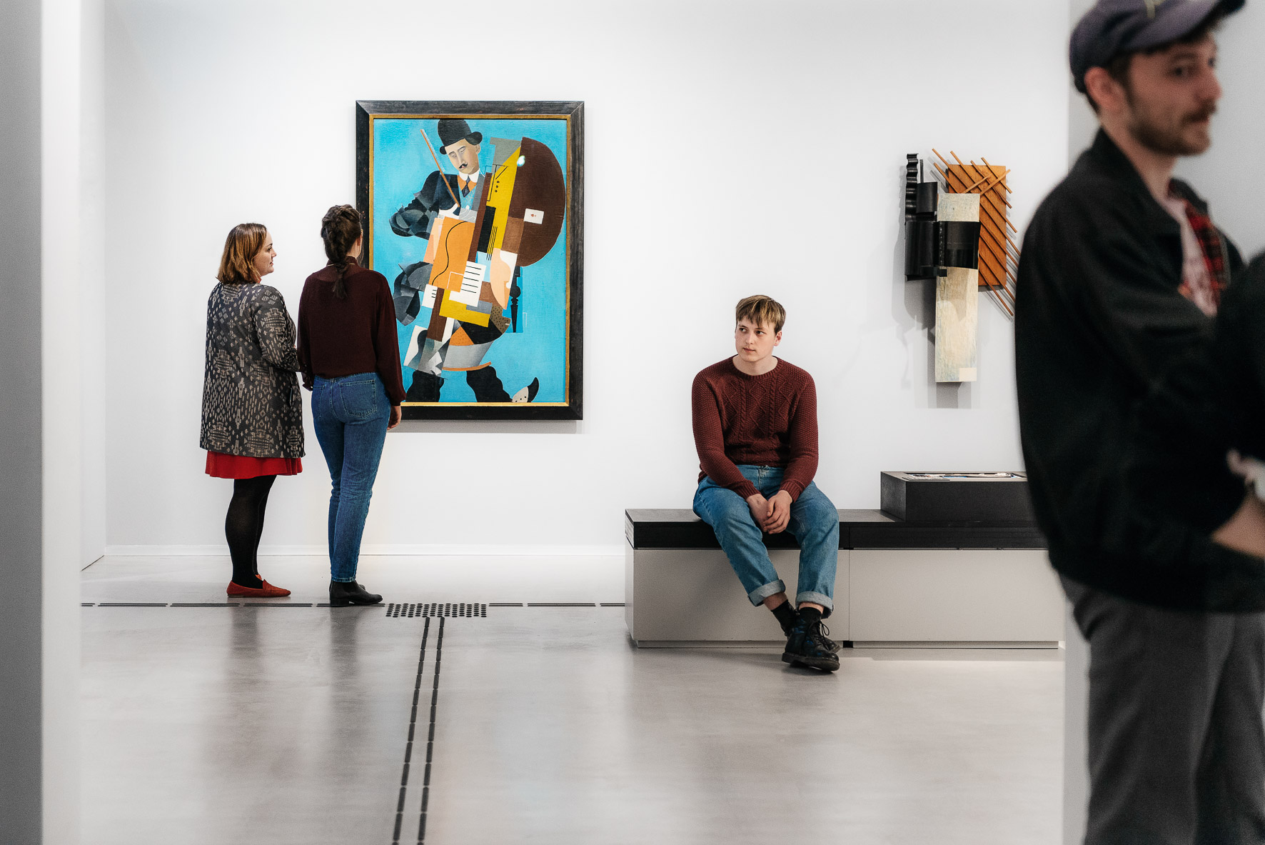 Photo: Several visitors stand and sit in the exhibition space and look at artworks.