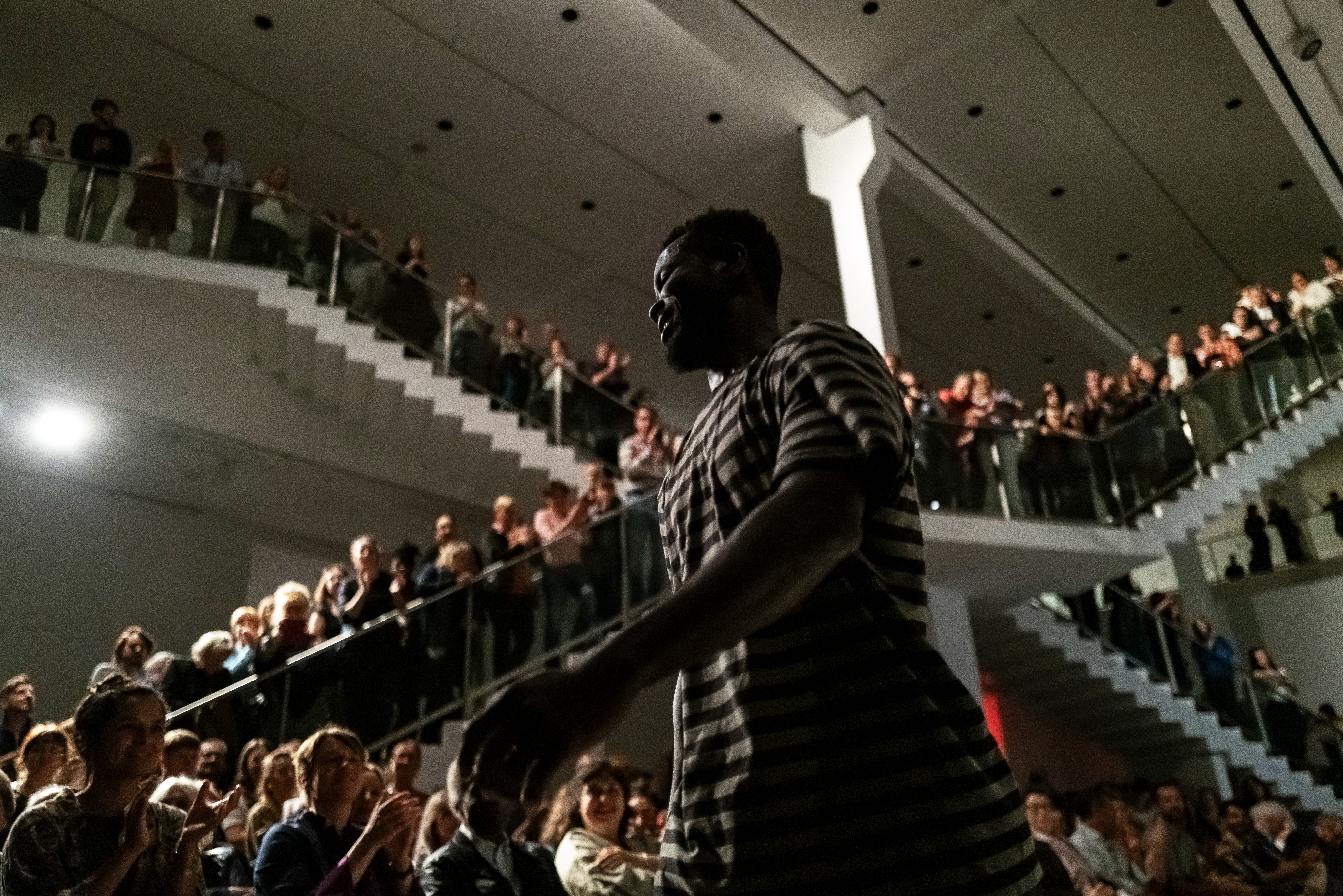 Photo: Meier Eden during his performance. In the background, many spectators can be seen sitting on chairs, standing and standing on two large staircases.