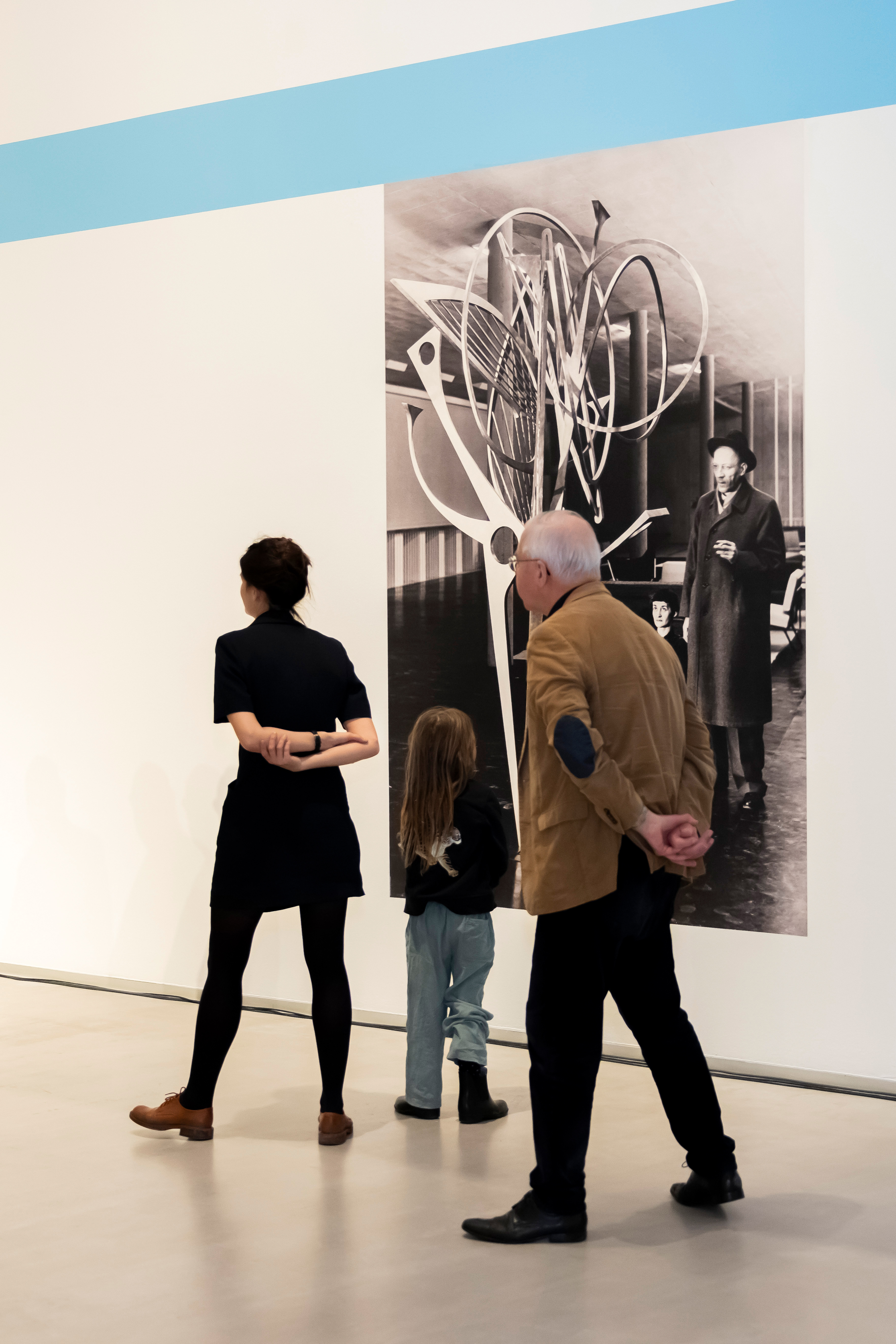 Photo: Three people stand in front of a black and white photographic wallpaper showing Hans Uhlmann next to one of his sculptures.